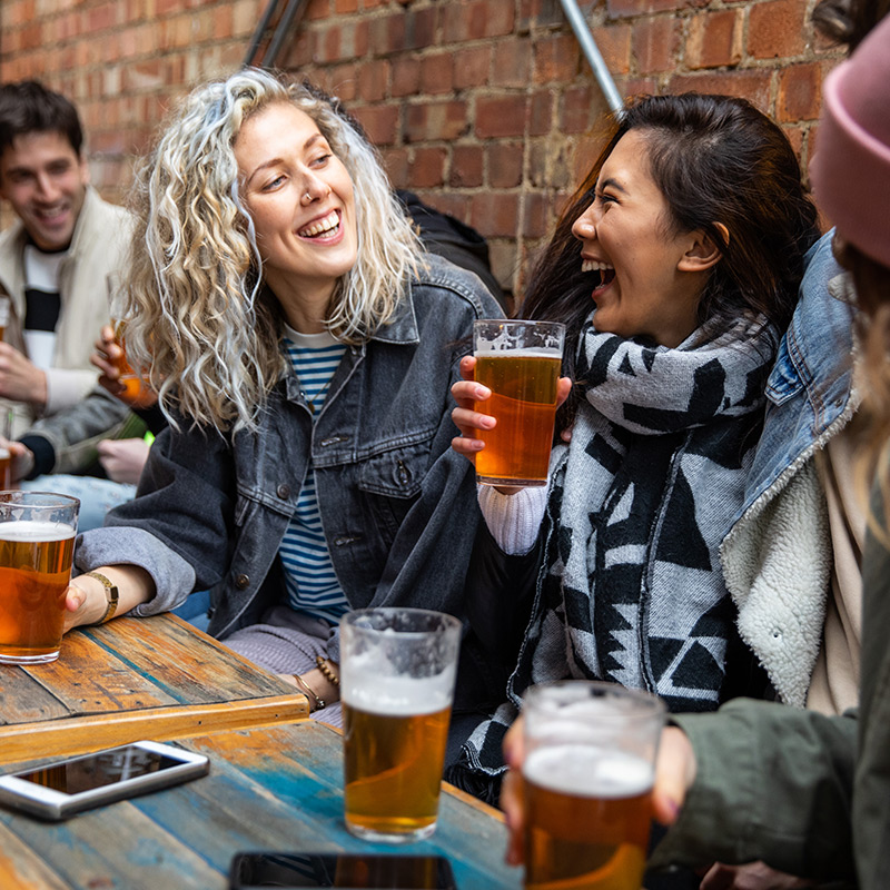 Two women with wide smiles as they hold a cold pint glass of amber beer