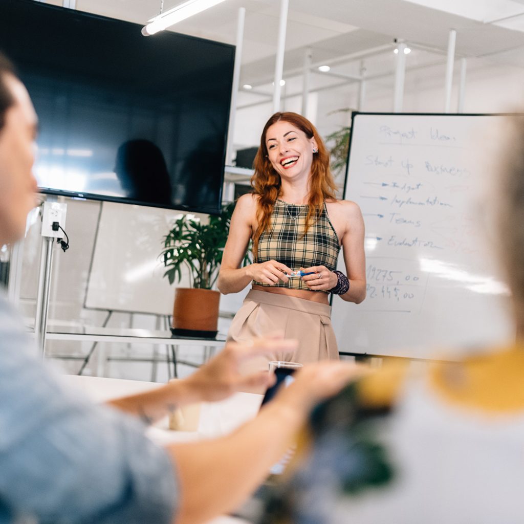 Woman smiling holding marker next to whiteboard